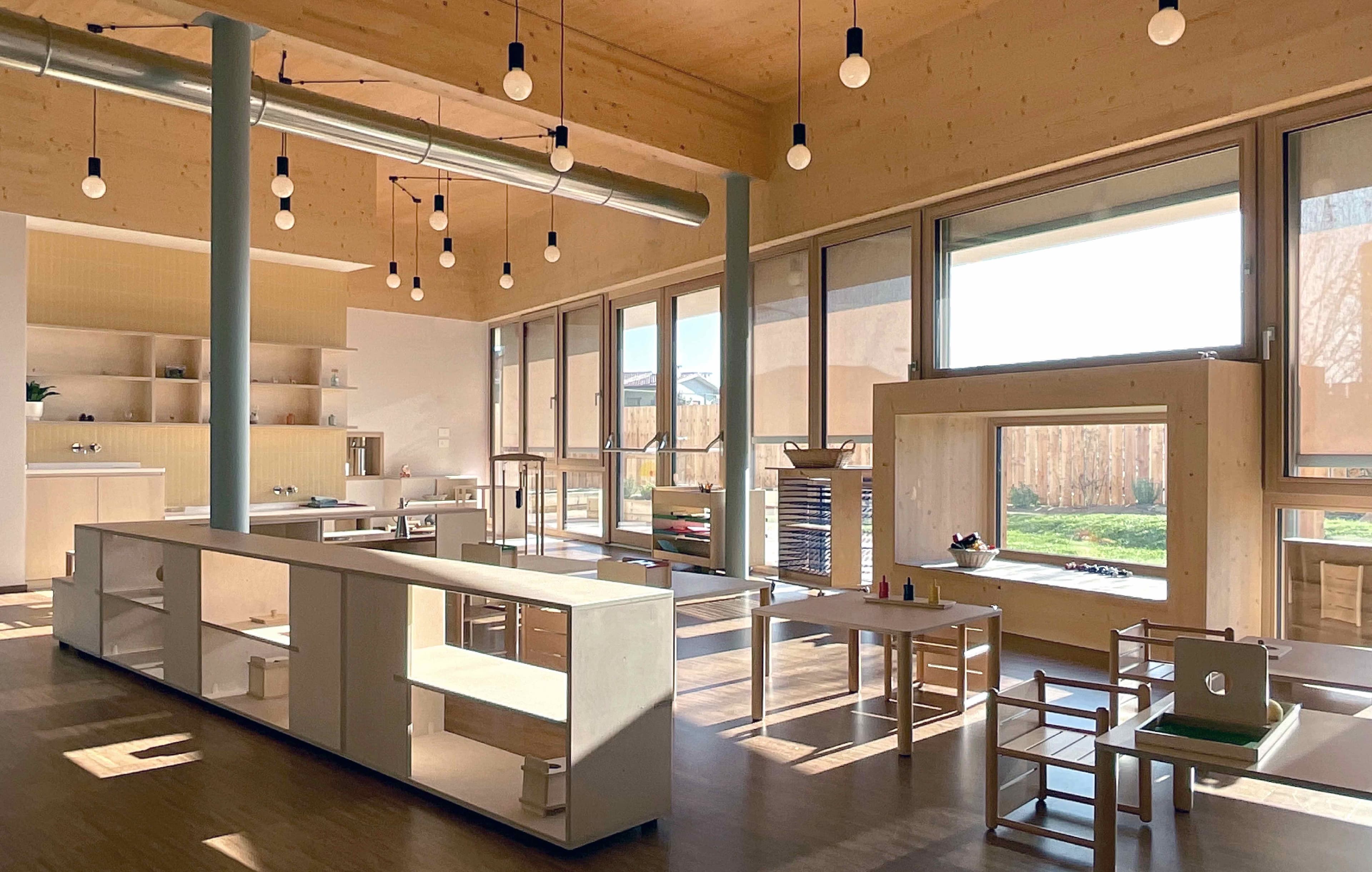 A Montessori environment with cabinets and chairs, lit by ceiling lamps.