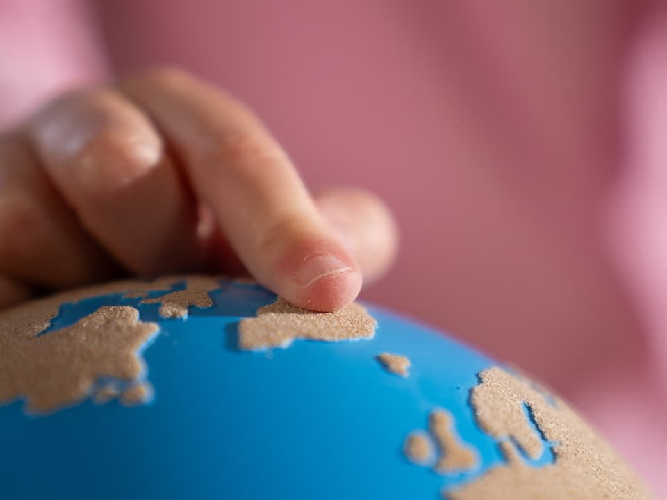A close-up of a child's finger touching a rough-smooth globe from Nienhuis.