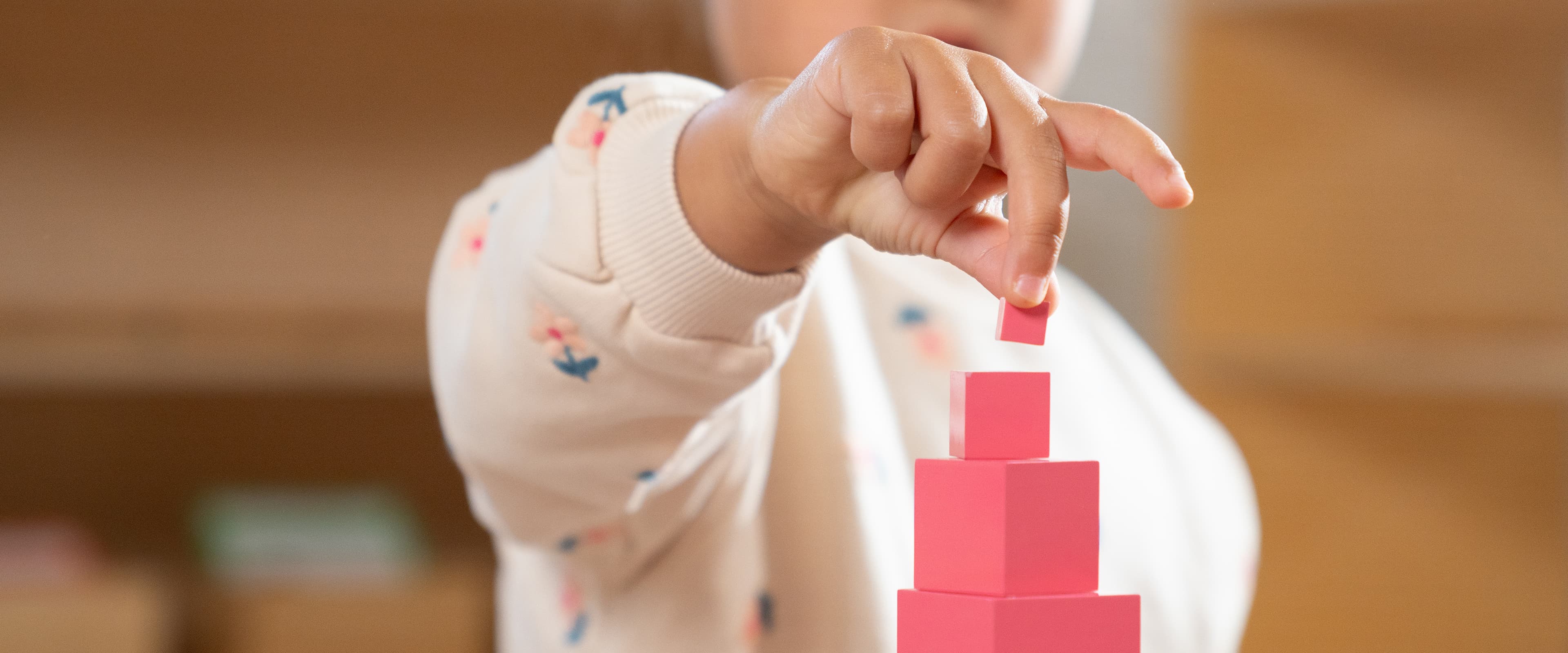 A child's hand stacking pink blocks from a Pink Tower.