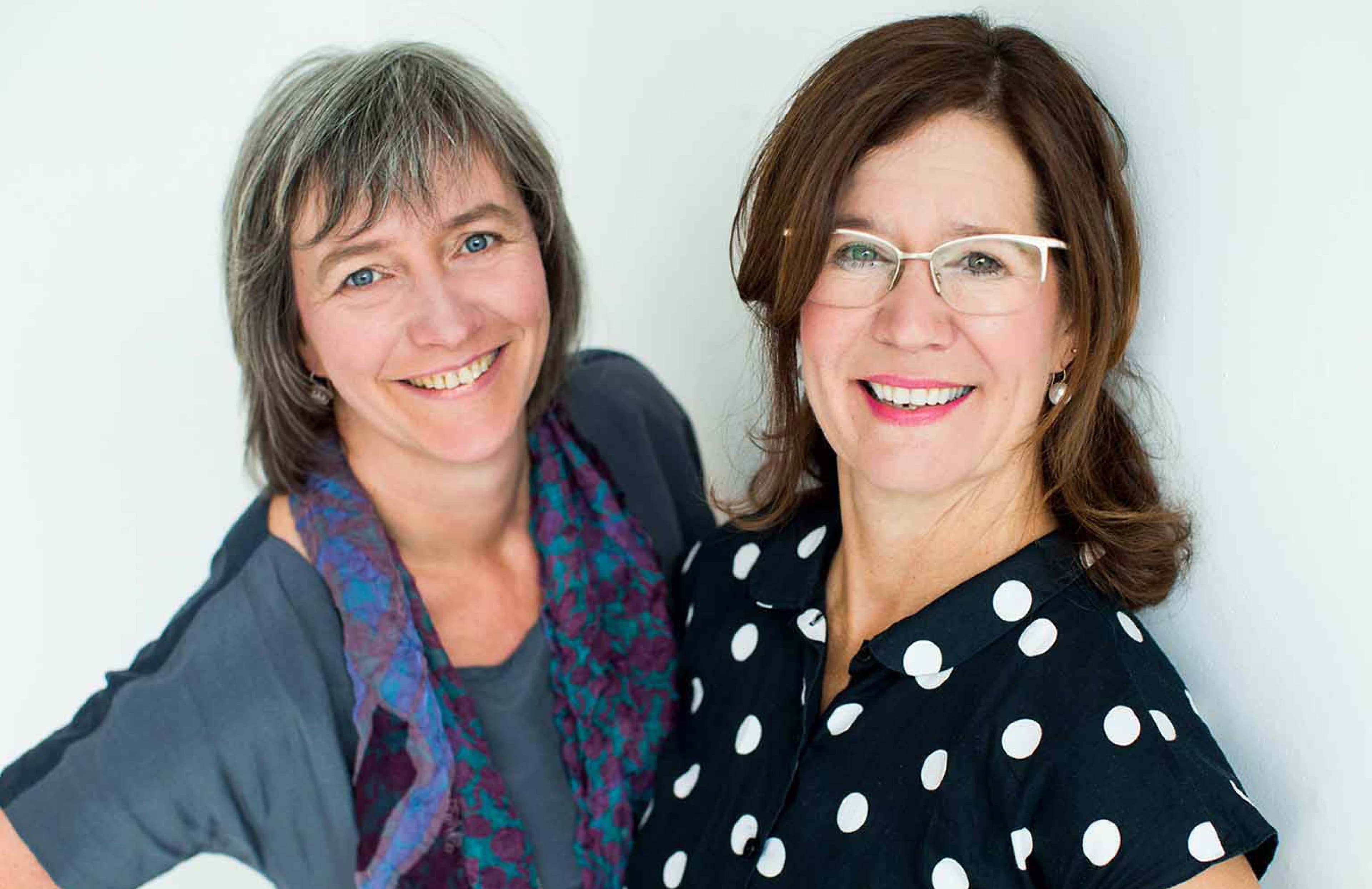 Zwei Frauen, die lachend in die Kamera schauen.